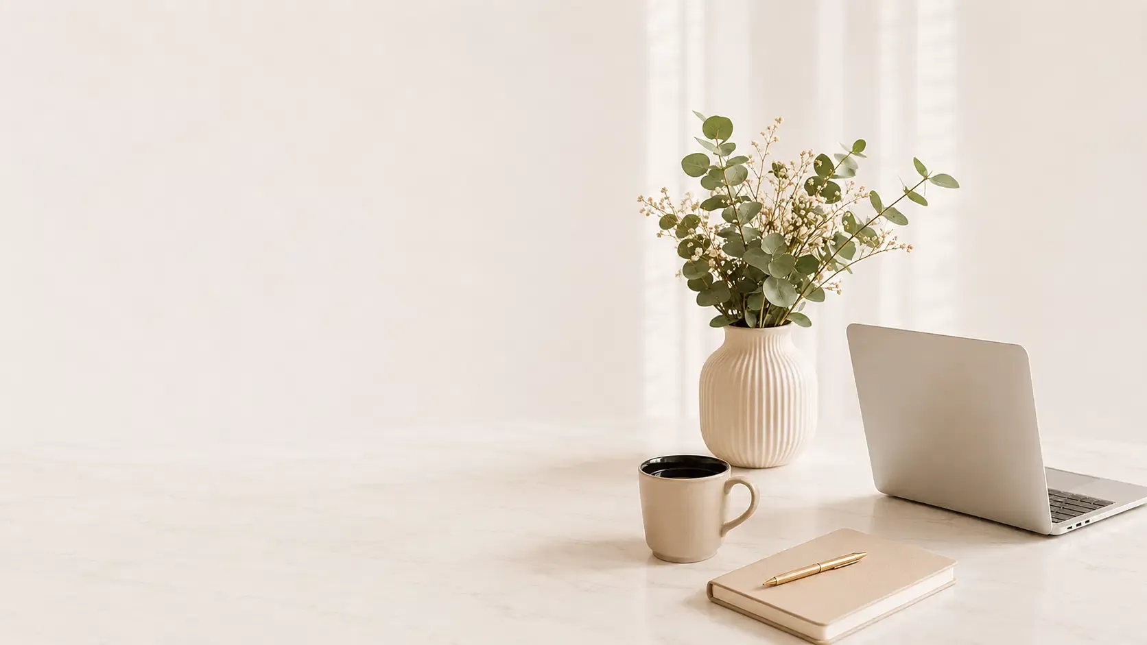 A calm marble desk with a laptop, notebook, coffee, and eucalyptus